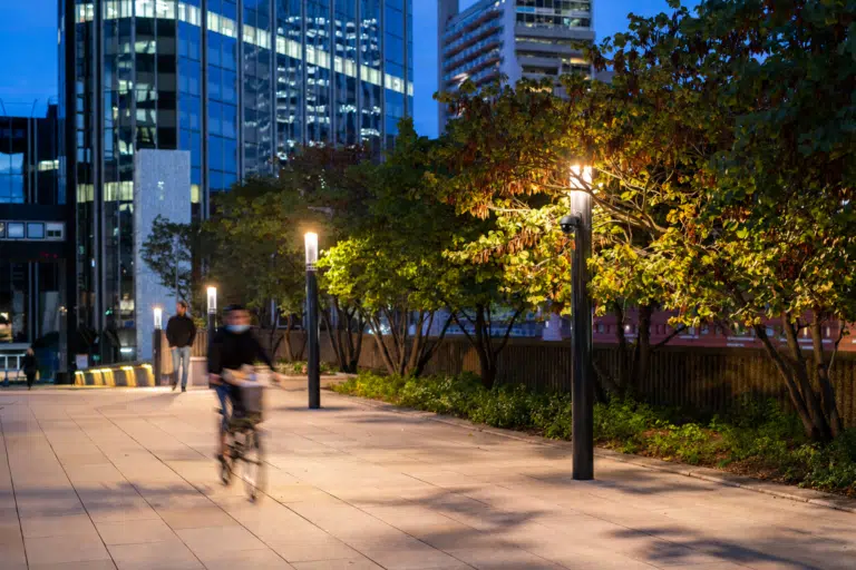 Ciclista e pedone percorrono un’area urbana illuminata, con telecamera integrata nel lampione.